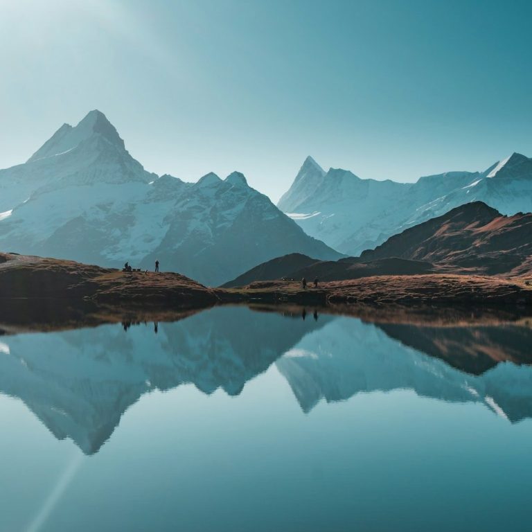 Berglandschaft mit reflektierenden Gipfeln in ruhigem Wasser und klarem Himmel.